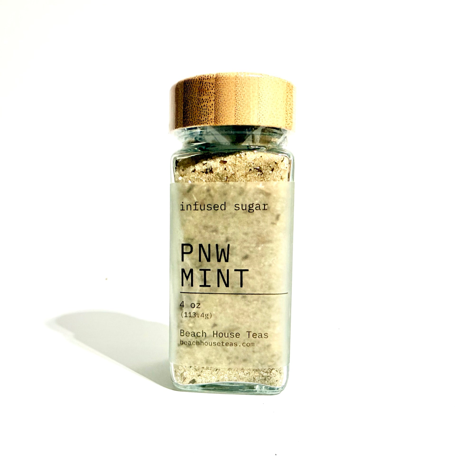 A clear glass jar of PNW Mint infused sugar with a metallic gold lid and a white label, set against a plain white background with a soft shadow.