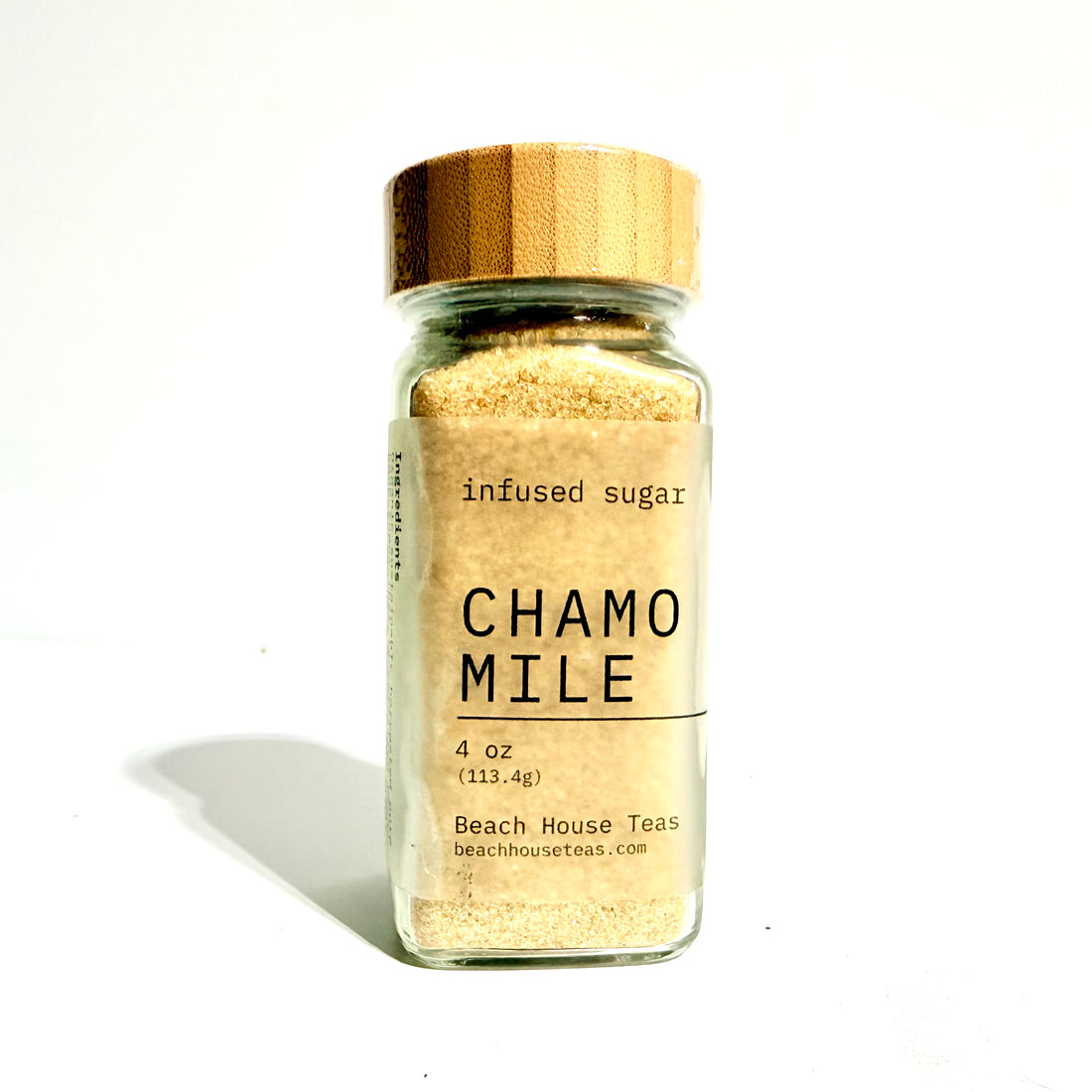 A clear glass jar of Beach House Teas Chamo Mile infused sugar with a light brown wooden lid, set against a plain white background with a soft shadow.