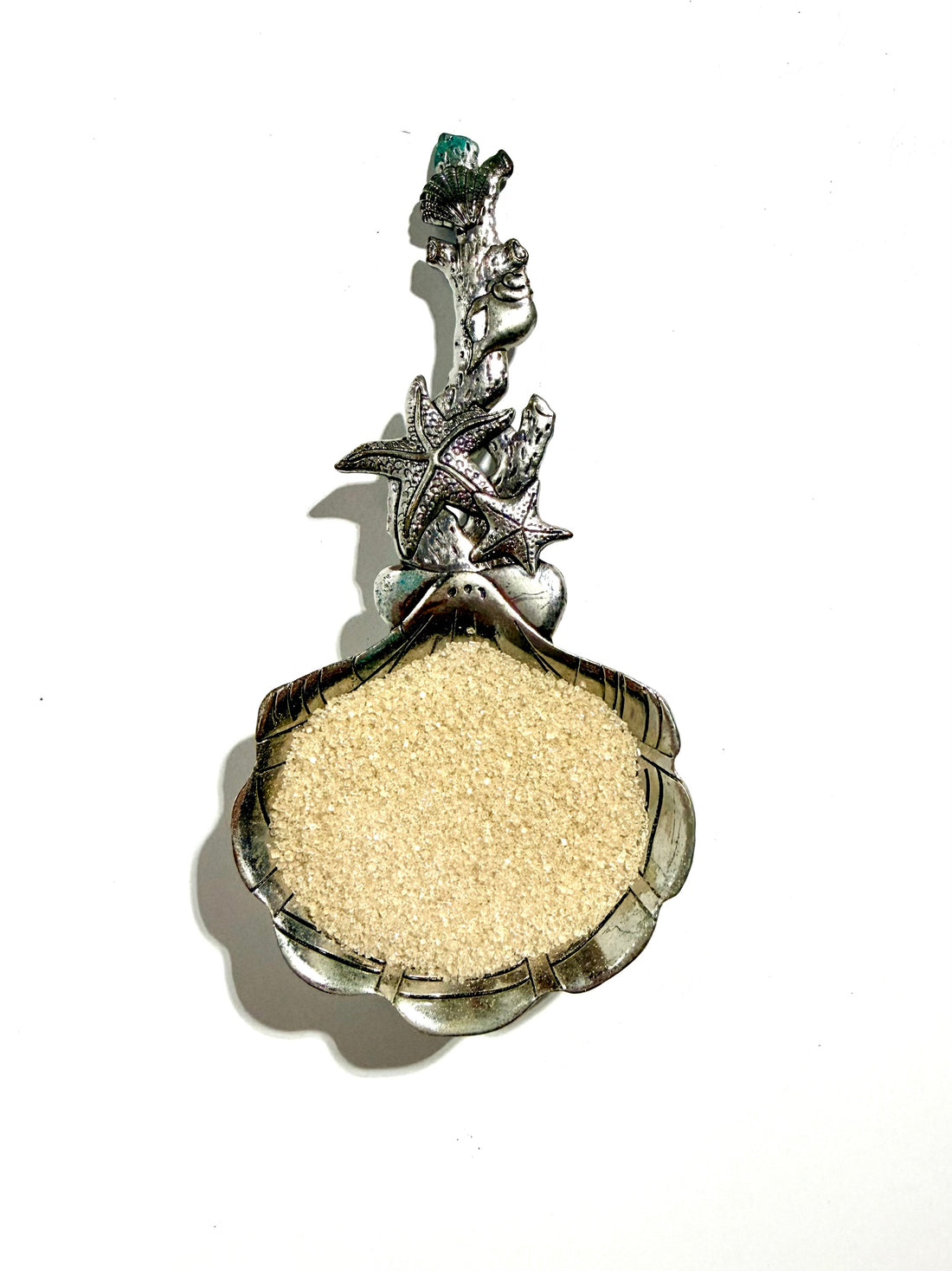 A silver-toned shell-shaped pendant or dish filled with light beige sand, featuring starfish and mermaid details on the bail, shown against a plain white background.