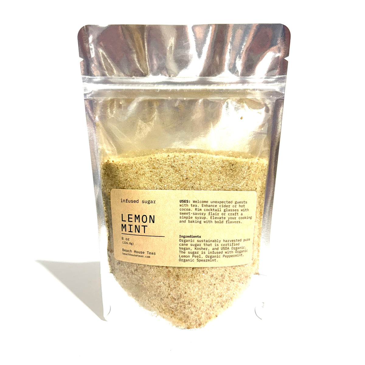 A stand-up resealable pouch of infused sugar labeled 'Lemon Mint' on a white background. The pouch is transparent and filled with pale yellow-beige granulated sugar, with a beige label and silver reflective packaging.
