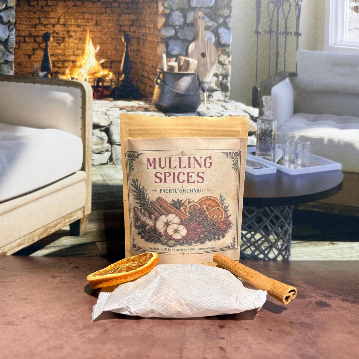 Pacific Orchard Mulling Spices pouch with a sachet, dried orange slices, and cinnamon stick beside a fireplace.