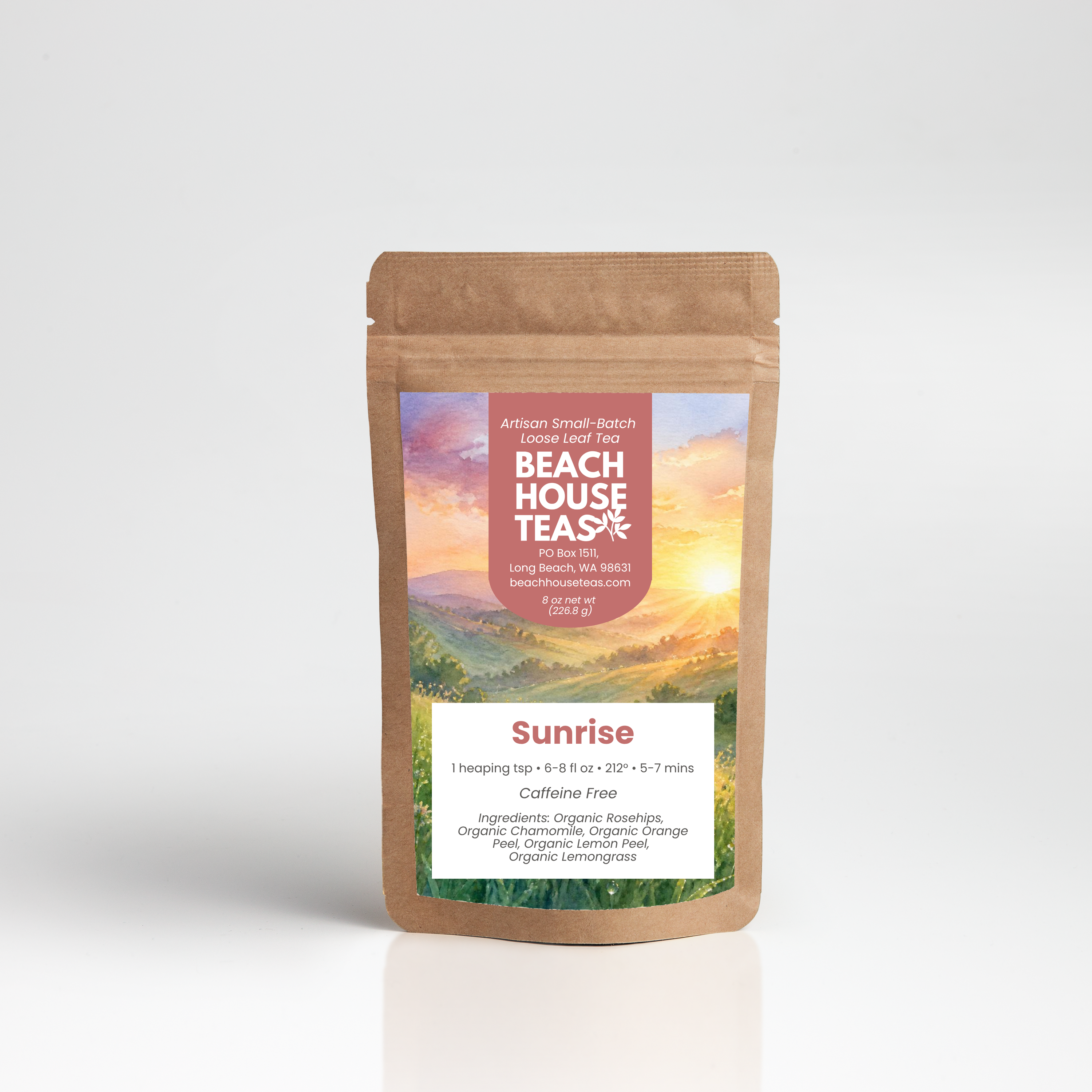 A stand-up kraft paper pouch of Beach House Teas Sunrise loose-leaf tea, featuring a colorful label with a sunset landscape and white text, set against a clean white background with a soft reflection.