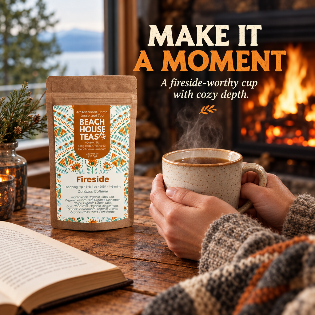 Hands holding a steaming tea mug beside a Fireside pouch, open book and wool blanket near a glowing fireplace.