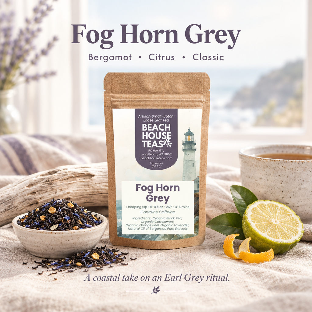 Fog Horn Grey tea pouch with loose leaf tea, citrus and a ceramic cup on linen beside driftwood.