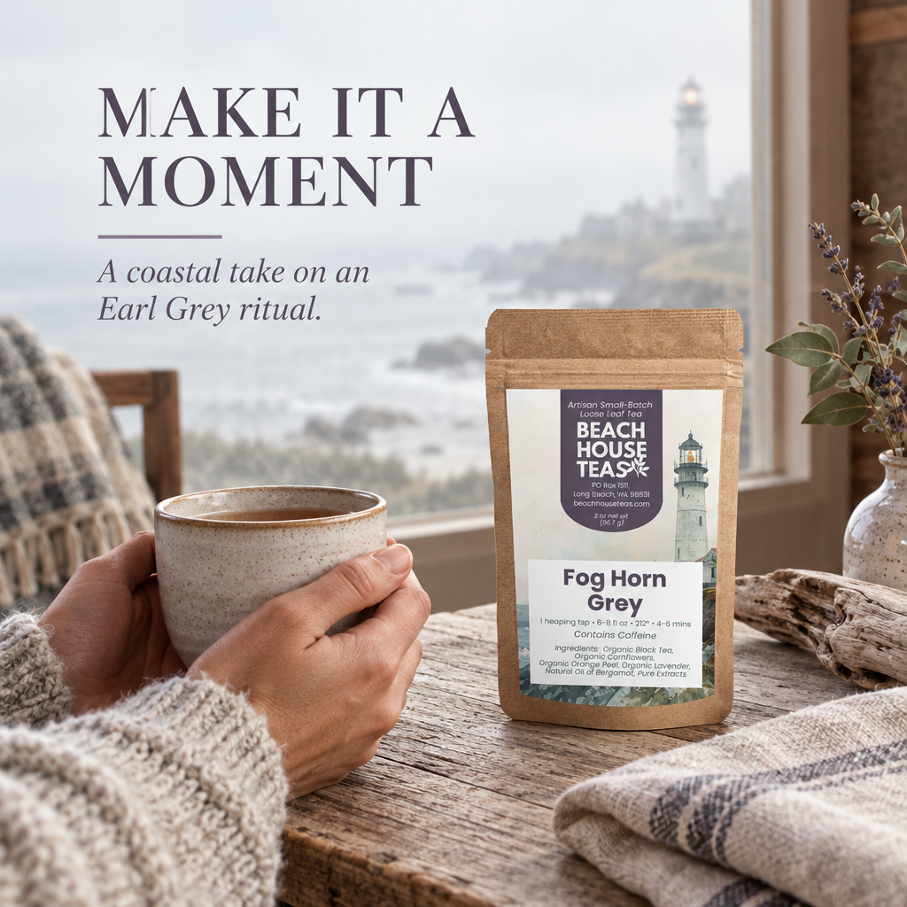 Hands holding a ceramic tea mug beside a Fog Horn Grey pouch at a window overlooking a foggy coast.