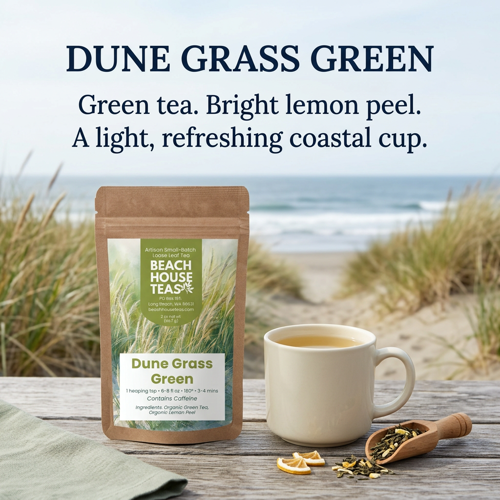 Dune Grass Green tea pouch beside a cream mug of golden tea, dried lemon peel and a wooden scoop on a coastal table overlooking dune grasses and surf. Green tea. Bright lemon peel. A light, refreshing coastal cup.