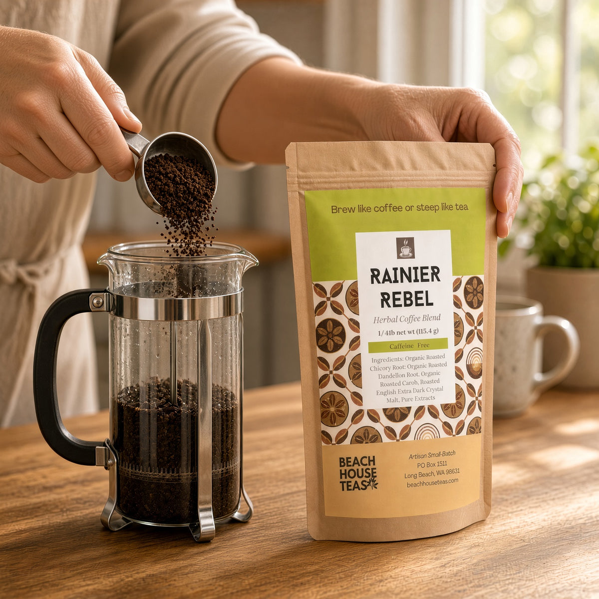 Person pouring Rainier Rebel herbal coffee from a metal scoop into a glass French press beside the kraft pouch